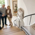 Modern stairlift on a residential staircase with people reviewing installation details before requesting a quote.